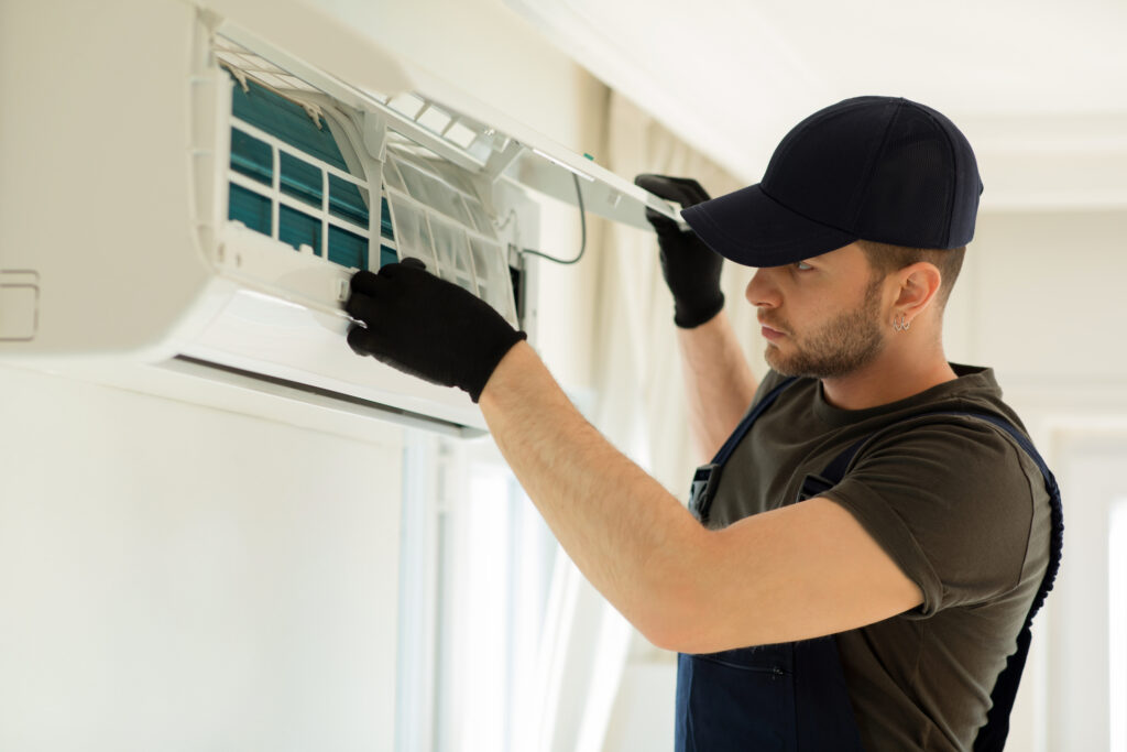 A man wearing a hat and gloves repairs an air conditioner.