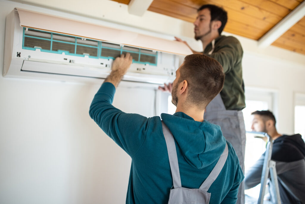 Two technicians working together on an air conditioning unit, tools in hand.