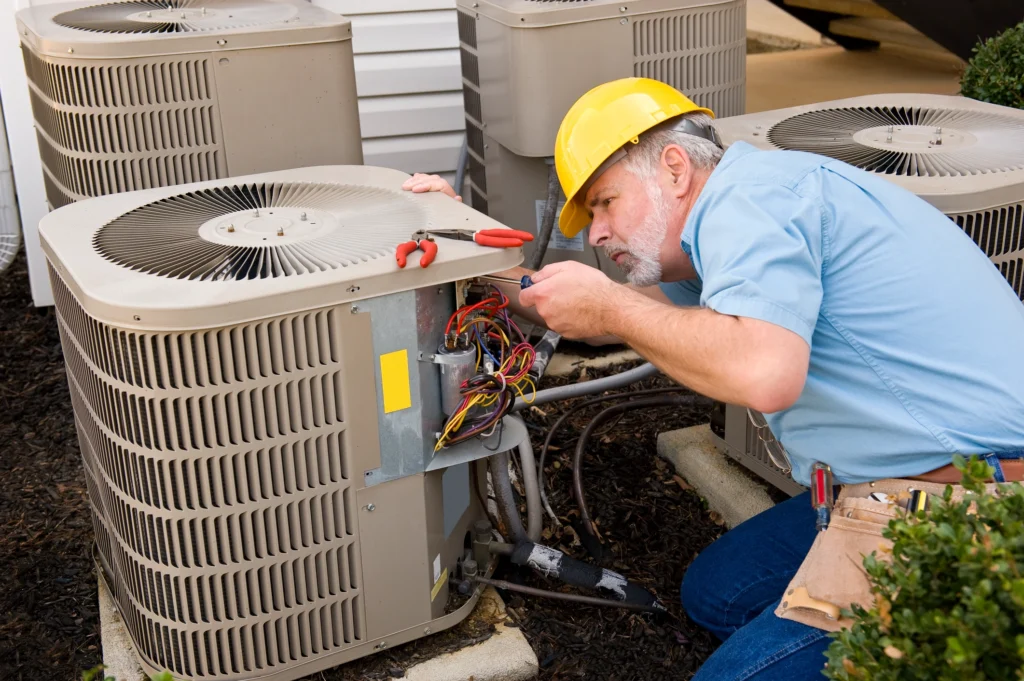 A man in a hard hat repairs an air conditioner, focused on his work.